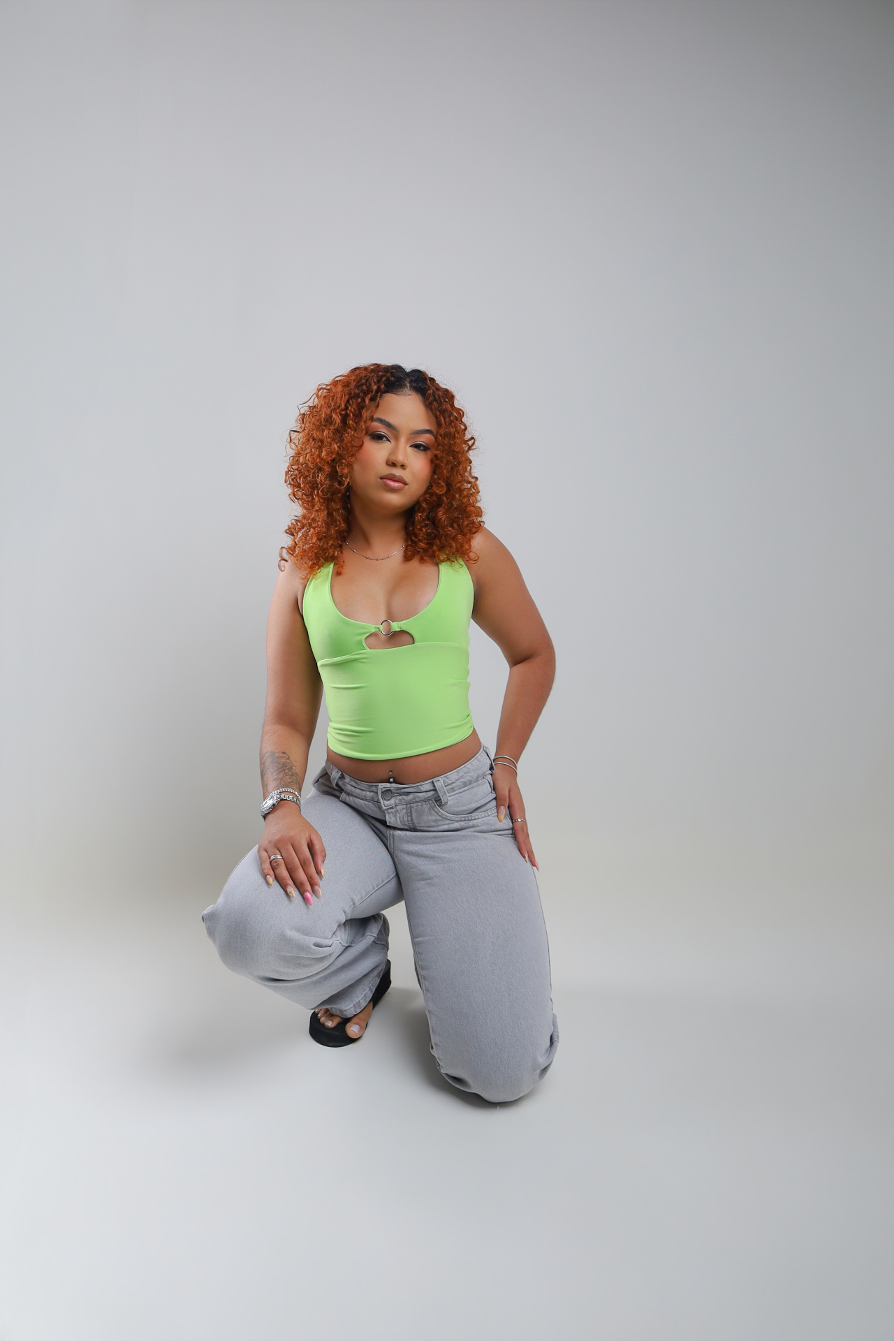 Gabrielly Vasconcelos em top verde e calça jeans cinza em fundo neutro